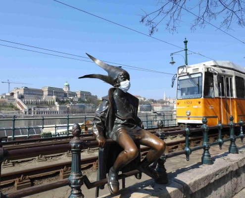 Photo taken by us of the Little Princess statue wearing a mask with tram number 2 and the Royal Palace of Buda in the background